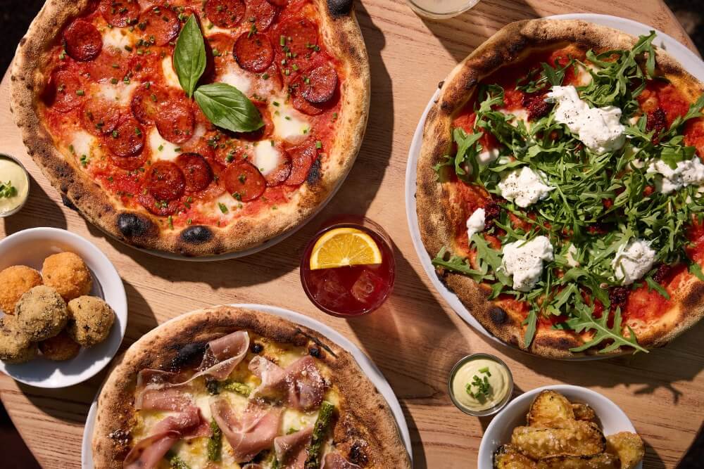 Fresh sourdough pizzas served on a wooden table with cocktails